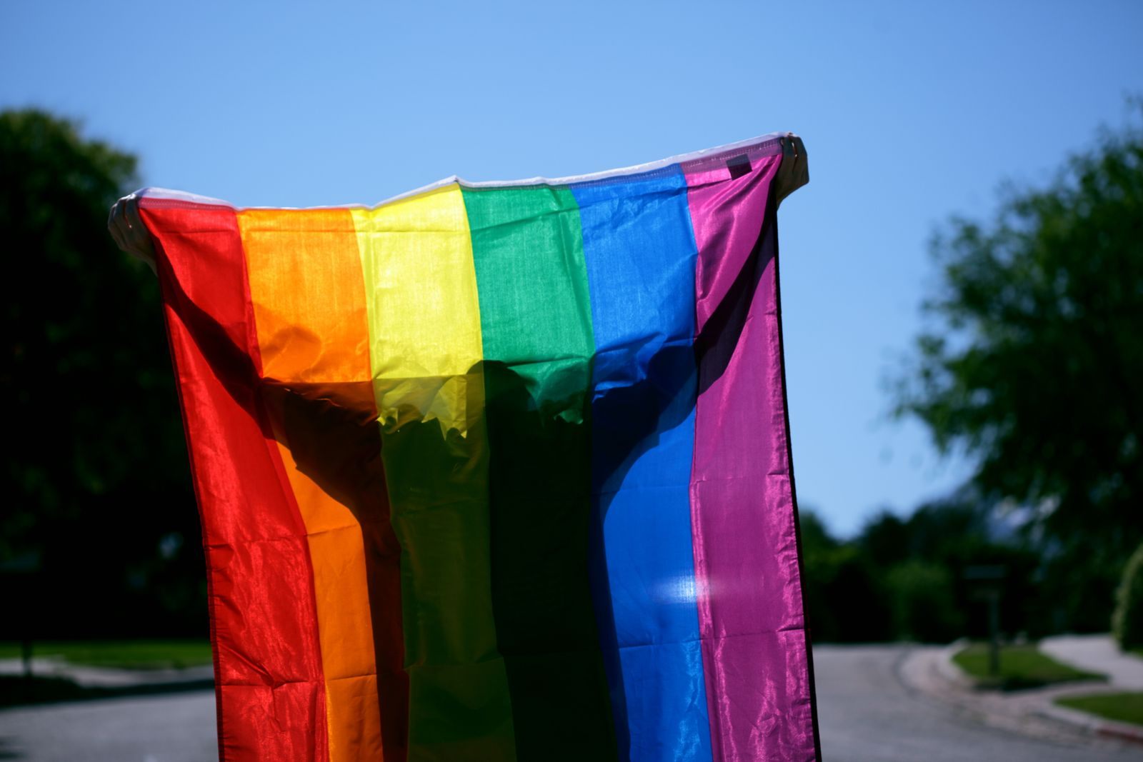 Rainbow pride flag held up outdoors against a blue sky, for LGBTQ+ group cruises 2027