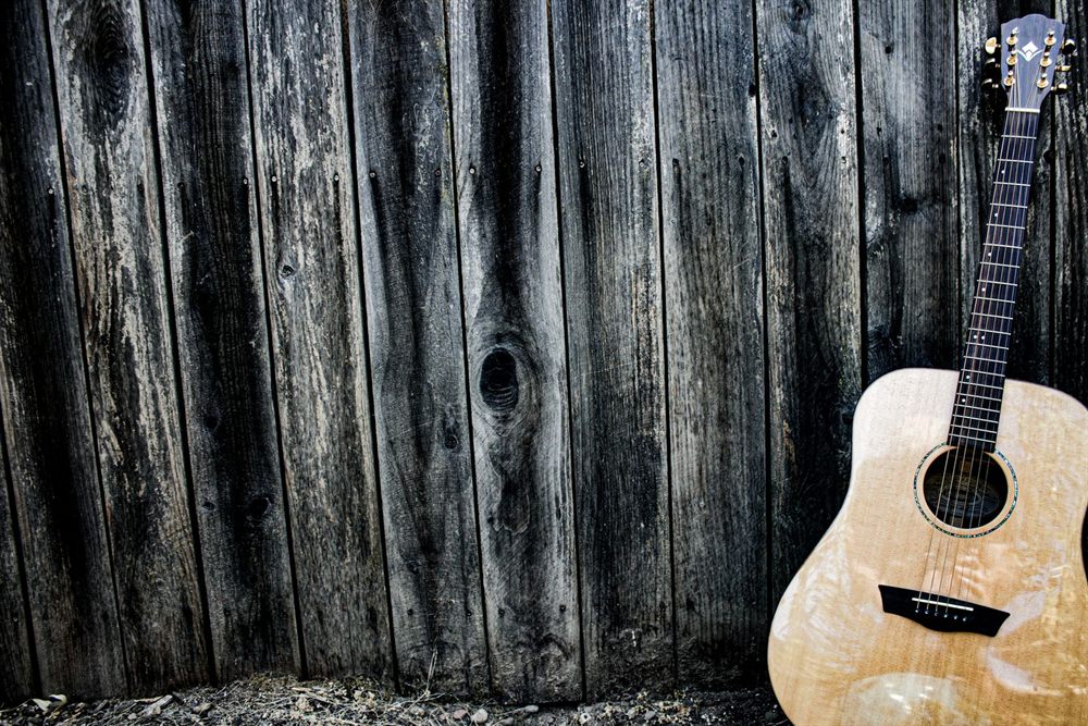 Acoustic guitar leaning against a weathered wooden wall